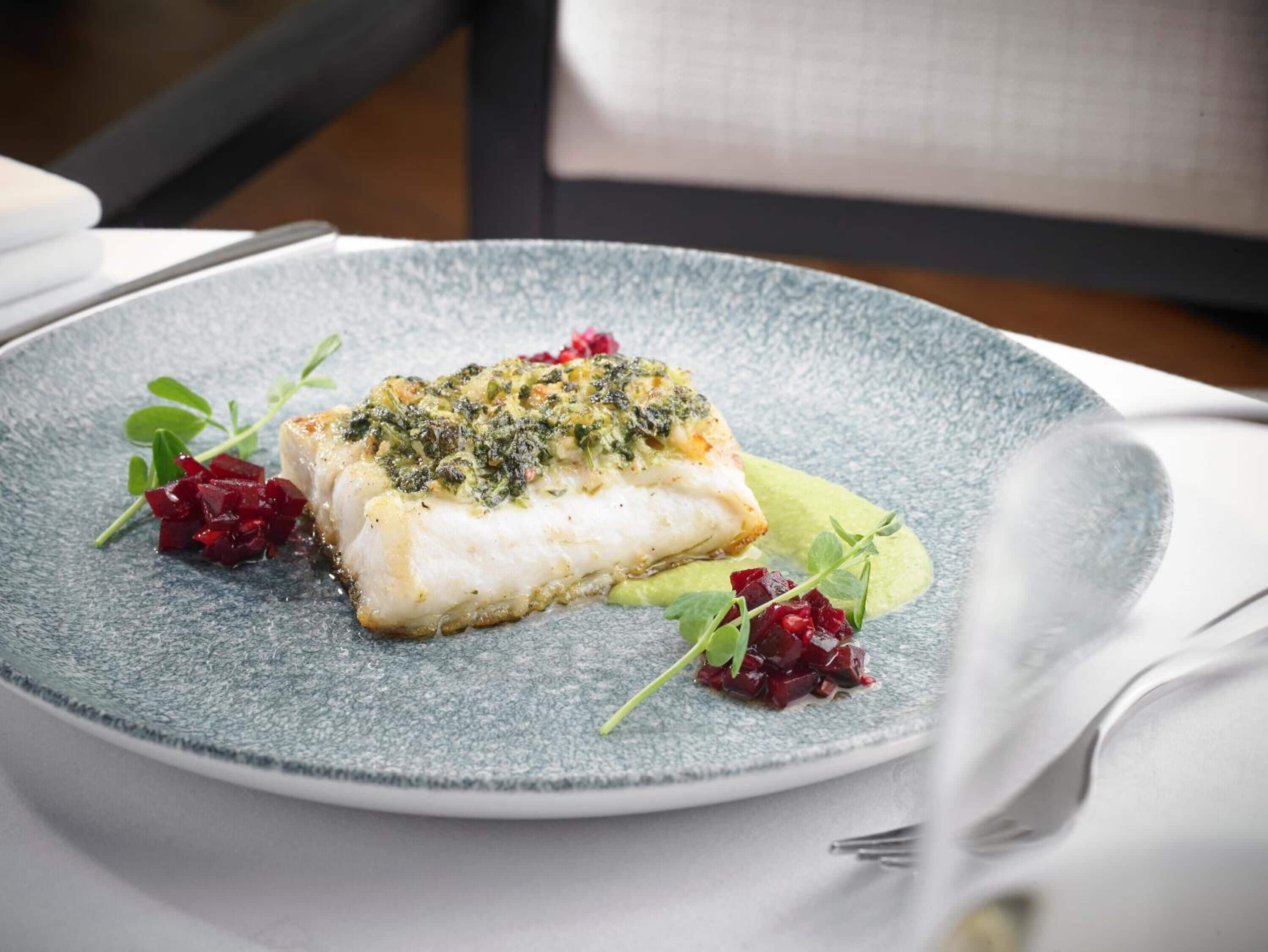 A plate with a piece of white fish topped with green herbs, accompanied by beetroot and greens.