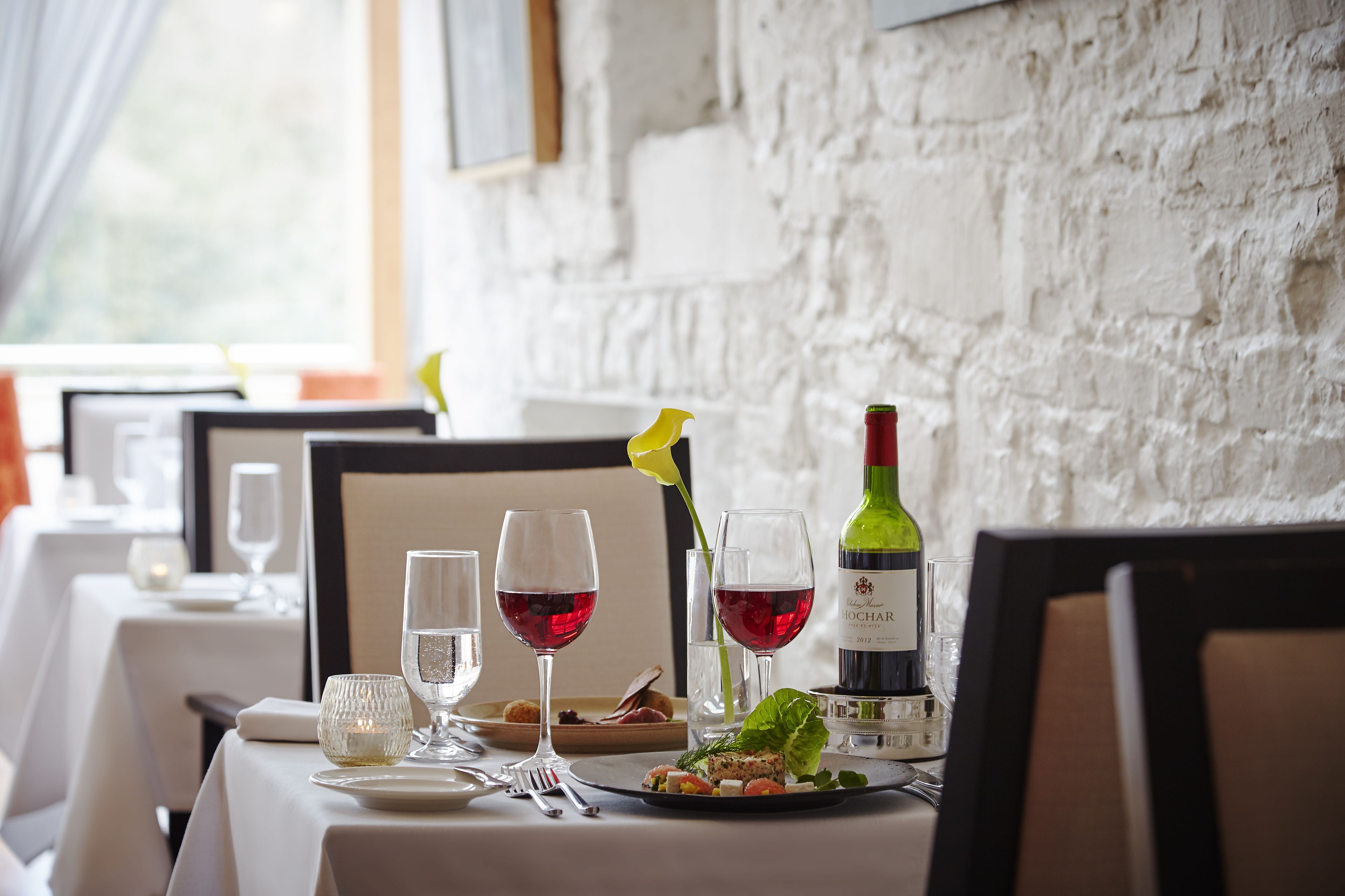 A dining table set with wine glasses, a bottle of wine, and a salad.