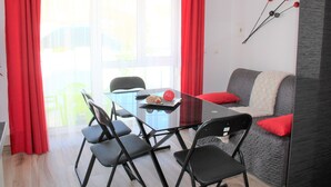 Ein Essbereich mit einem Glastisch, schwarzen Stühlen und einem grauen Sofa mit roten Kissen.
