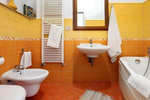 A bathroom with a bidet, sink, and bathtub, all with white fixtures, and a towel rack with towels.