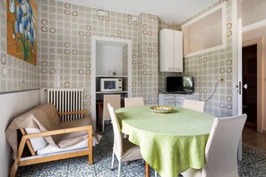 Un petit coin repas comprenant une table, des chaises, un banc, un four à micro-ondes, un téléviseur et des murs décorés de motifs.