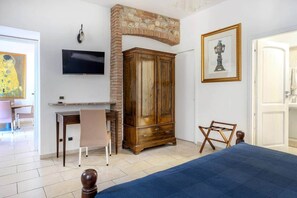 Une pièce comprenant un lit, une armoire en bois, un téléviseur fixé au mur et une porte donnant sur une autre pièce.