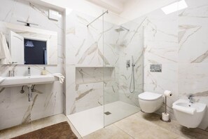 A modern bathroom with a marble shower, a toilet, a bidet, and a sink.