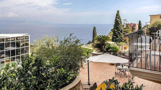 Una terraza con mobiliario exterior, vistas al mar y vegetación circundante.