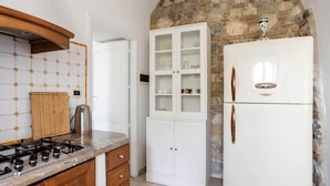 Una cocina con estufa a gas, armarios de madera, un refrigerador blanco y una pared de piedra.