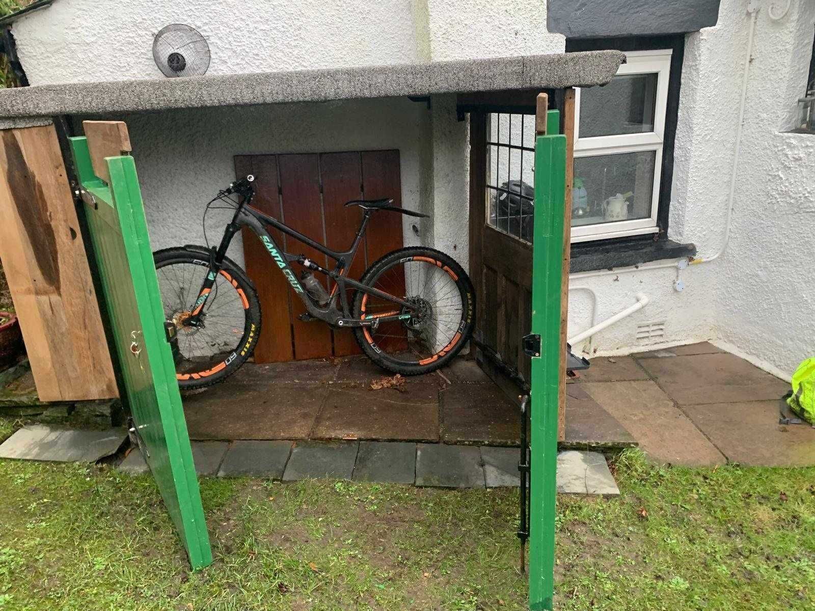 En cykel låst fast under en trækonstruktion med et vindue og en dør i baggrunden.