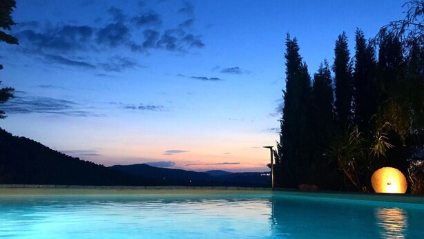 Una piscina con vistas al atardecer, rodeada de árboles y una lejana cadena montañosa.