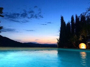 A swimming pool with a sunset view, surrounded by trees and a distant mountain range.