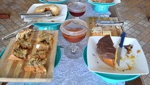 A dining area with a long table set with various dishes and drinks, surrounded by chairs and tables with floral tablecloths. - Icarai Palace Hotel e Pousada (Poços de Caldas)