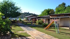 A residential area with a paved pathway, a playground with a slide, and houses with a hilly backdrop. - Icarai Palace Hotel e Pousada (Poços de Caldas)
