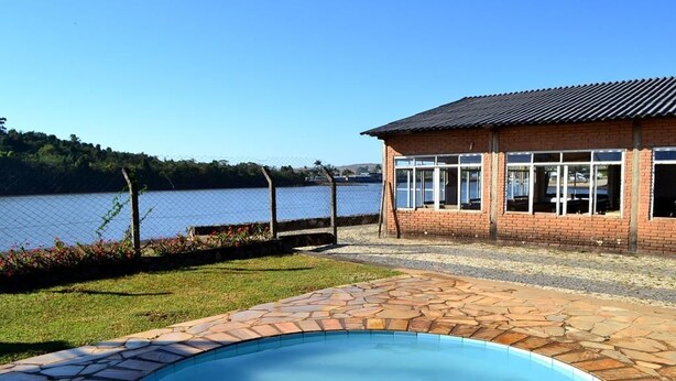 A swimming pool with a stone border, a brick building with large windows, and a view of a lake. - Icarai Palace Hotel e Pousada (Poços de Caldas)