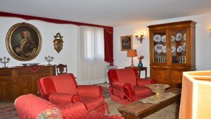 A room with a large portrait, a cabinet with dishes, and red upholstered furniture.