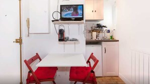 Eine kleine Küche mit einem Fernseher über einem weißen Tisch und roten Stühlen.