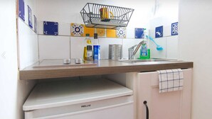 Eine Küche mit einer Holzausziehtheke, einem Spülbecken und einem Geschirrständer. Auf der Theke liegen verschiedene Küchenutensilien, darunter eine Flasche Spülmittel und ein Metallbehälter.