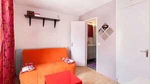 Ein kleiner, farbenfroher Raum mit einem roten Tisch, einem orangefarbenen Sofa und einer weißen Tür.