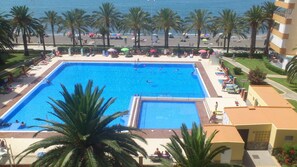 Ein großer Swimmingpool, umgeben von Palmen und Strandstühlen, mit Blick auf den Strand und den Ozean im Hintergrund.