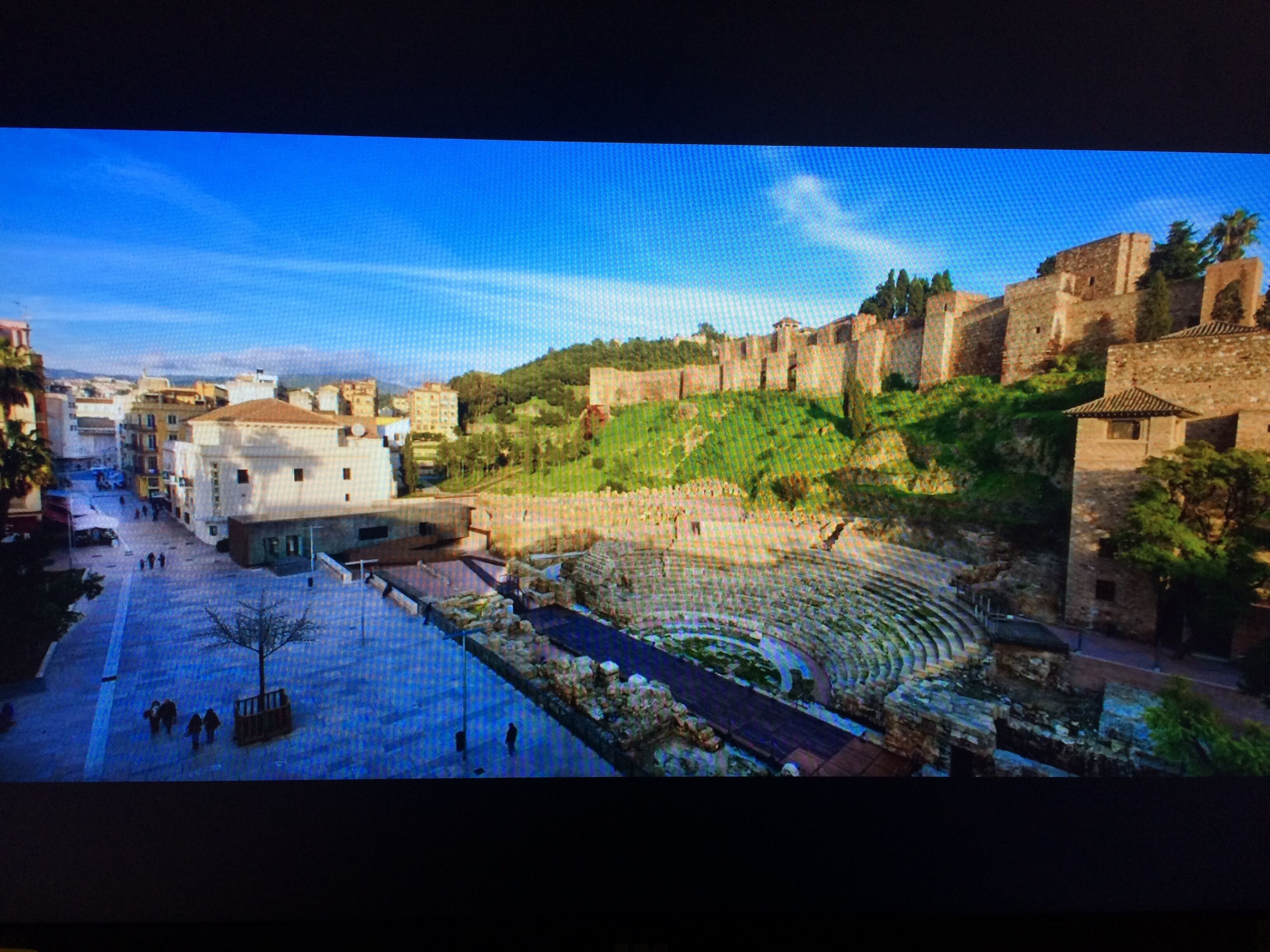 A historical site with ancient ruins, a central open space, and surrounding buildings.