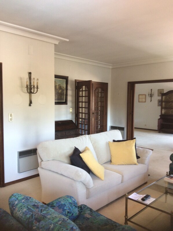 A living room with a white sofa, patterned armchairs, a glass coffee table, a candelabra, and a door with glass panels.