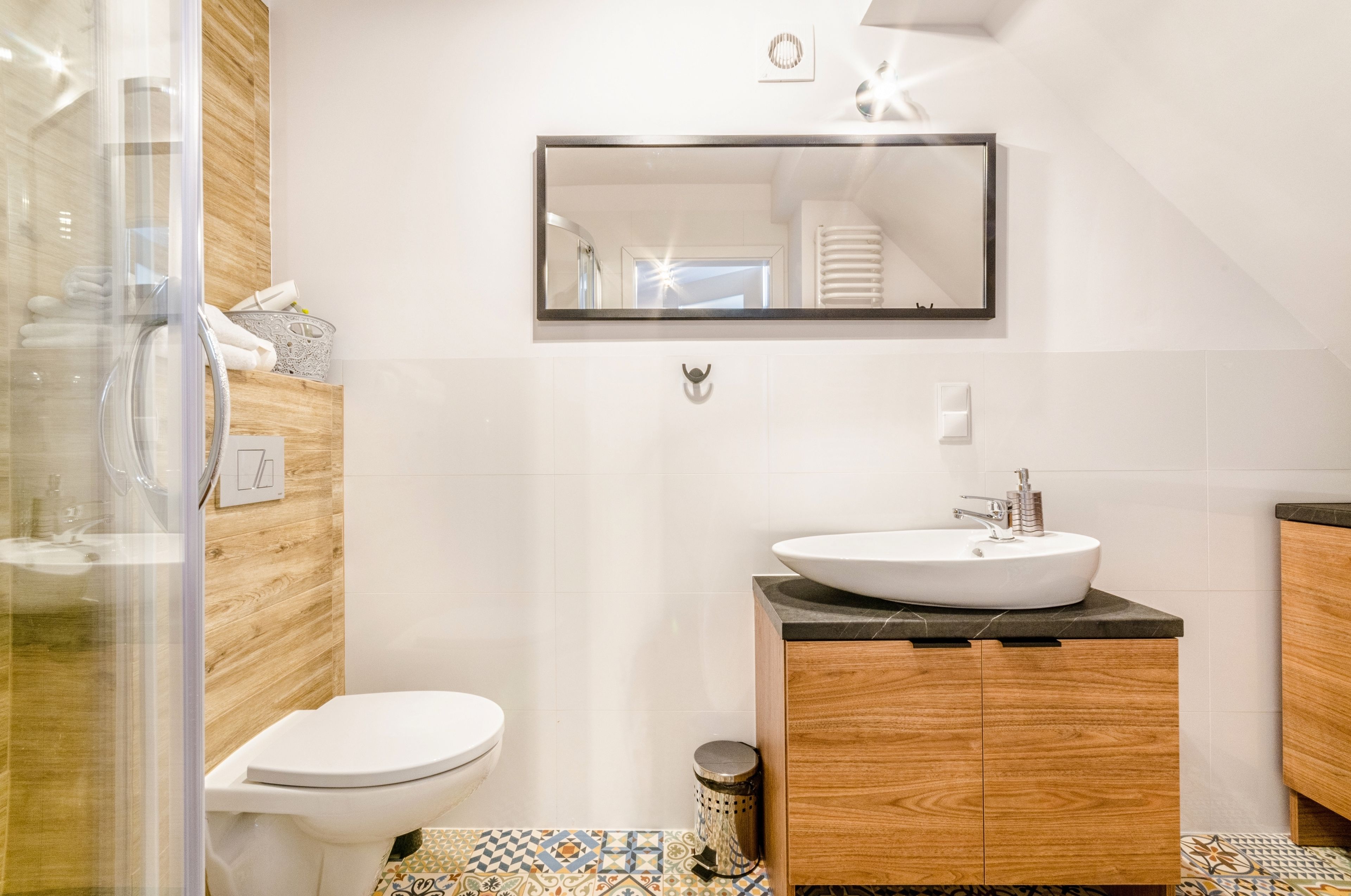 A modern bathroom with a glass shower enclosure, a white toilet, a wooden vanity with a sink, and a mirror above the vanity.