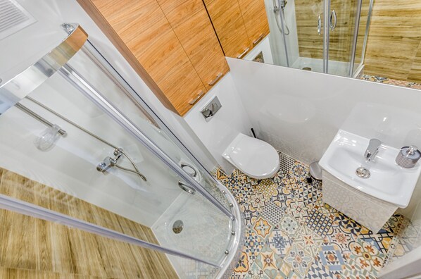 A modern bathroom with a glass shower enclosure, a white toilet, and a sink with a patterned tile floor.