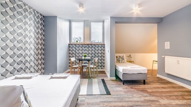 Habitació moderna amb llit, taula petita amb cadires, finestra i radiador.