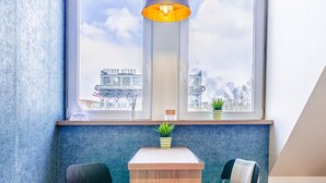 Una habitació petita amb una taula de fusta, dues cadires, una finestra amb vista a edificis i una làmpada penjant.