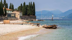 Una playa de guijarros con un banco de madera, un muro de piedra y un edificio con balcón con vistas al mar.