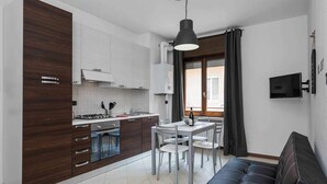 Una cocina moderna con armarios de madera oscura, un comedor con mesa y sillas, y un sofá de cuero negro.