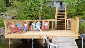 A wooden deck with colorful Adirondack chairs and a metal railing.