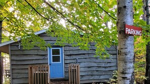 A rustic cabin with a blue door, a wooden bench, and a 'PARKING' sign.