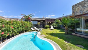 Une piscine à l’eau d’un bleu limpide, entourée d’une pelouse bien entretenue et, au fond, d’un bâtiment en pierre.