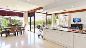 Une cuisine moderne avec des meubles blancs, un plan de travail en marbre et un coin repas agrémenté de chaises et d’une table en osier.