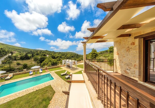 A poolside area with a stone pool, lounge chairs, and a pergola overlooking a scenic landscape.