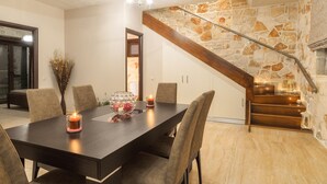 A dining area with a dark wooden table, six chairs, and a lit candle centerpiece. A staircase with stone walls and wooden steps is visible in the background.