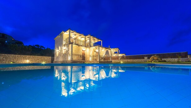A large, illuminated building with a swimming pool in front.