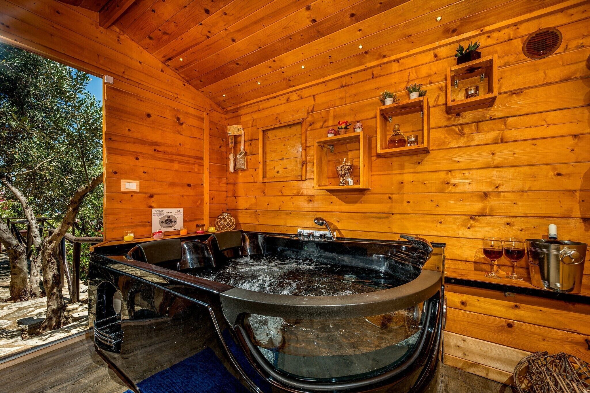 Eine Holzhütte mit Whirlpool, Regalen mit Dekorationsgegenständen und Blick auf Bäume.