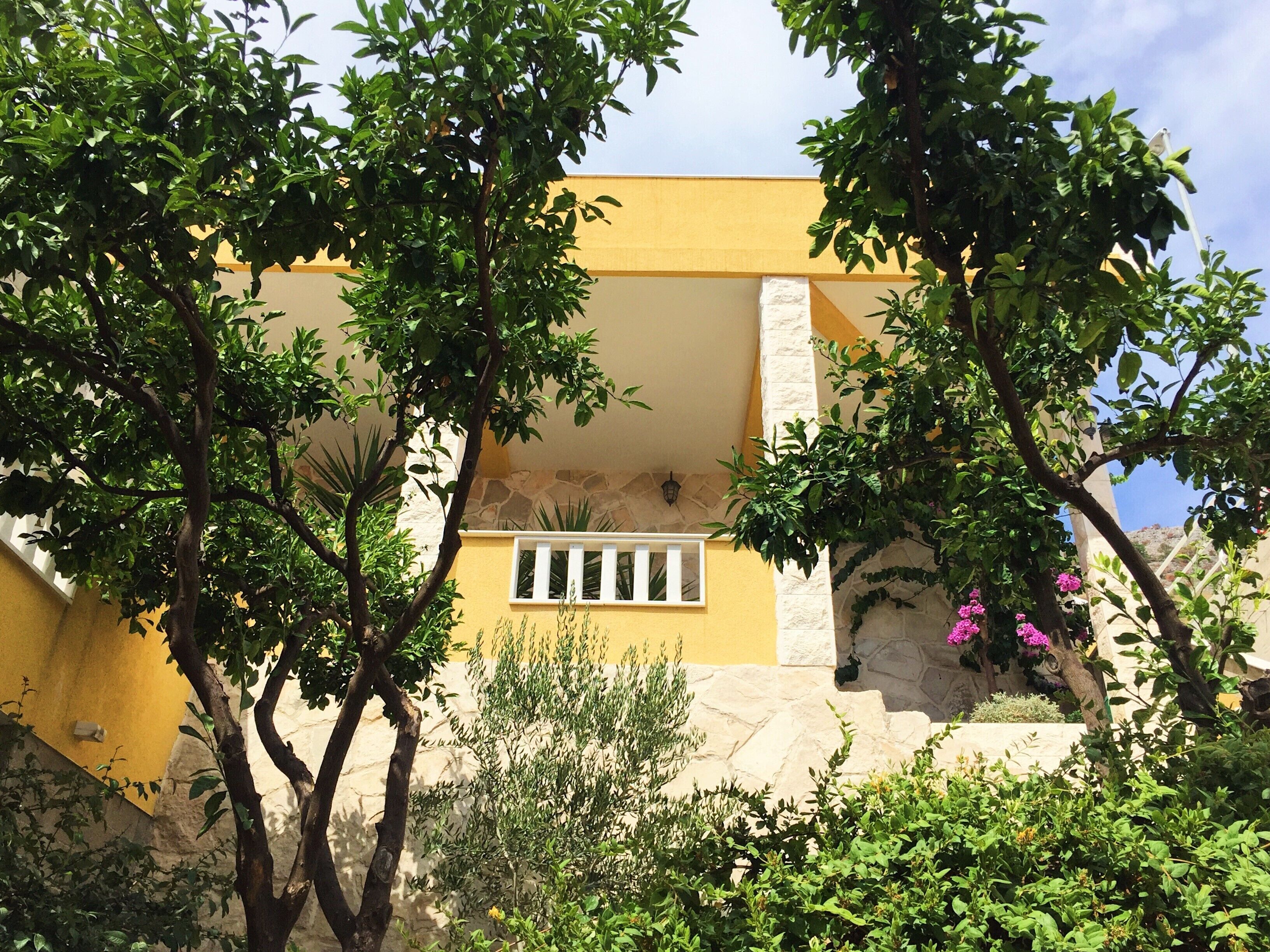 A building with a yellow facade, stone accents, and a window with white shutters.