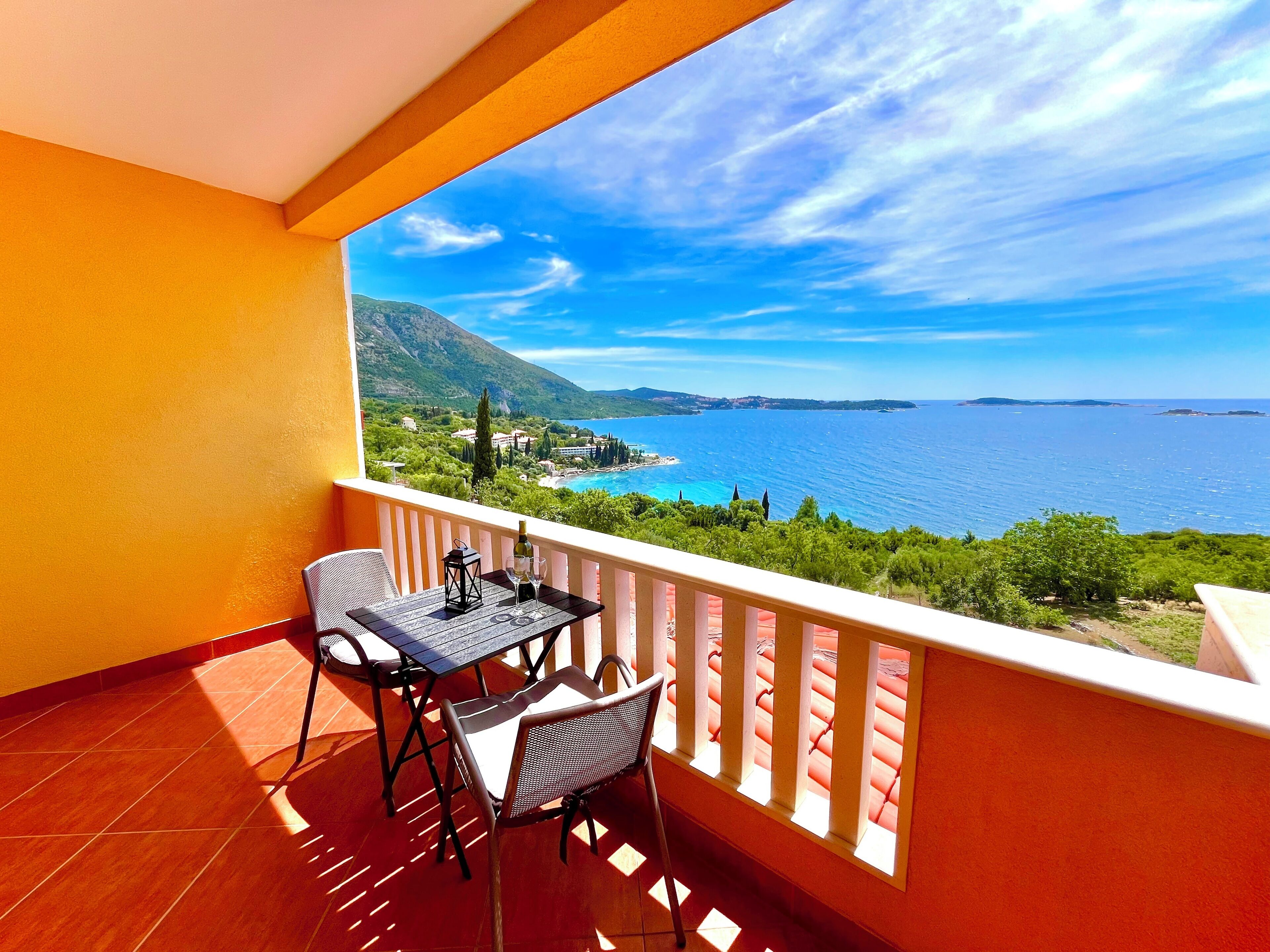 A balcony with a table and chairs, overlooking a coastal landscape with a clear sky.