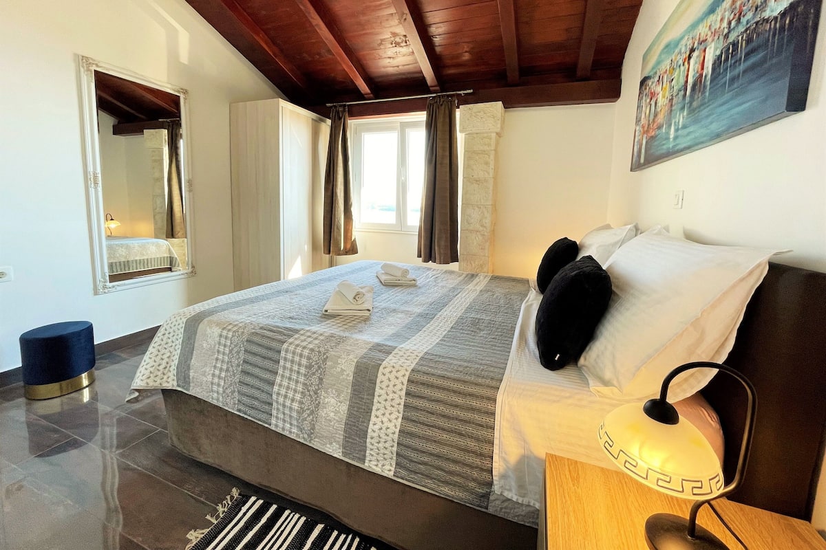 A bedroom with a large bed, a nightstand with a lamp, a mirror, and a painting on the wall.