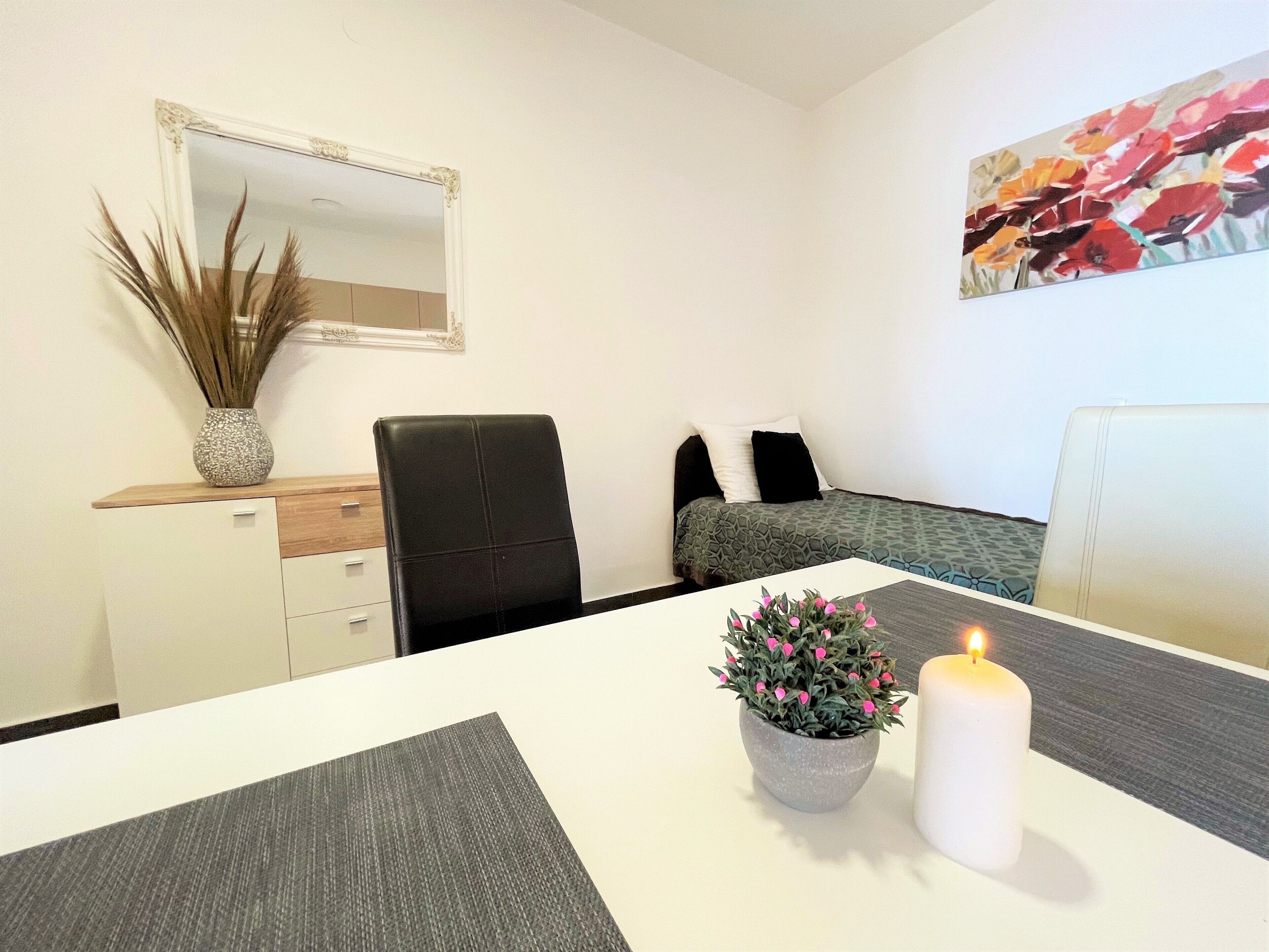 A modern bedroom with a bed, a chair, a desk, a mirror, and a painting on the wall.