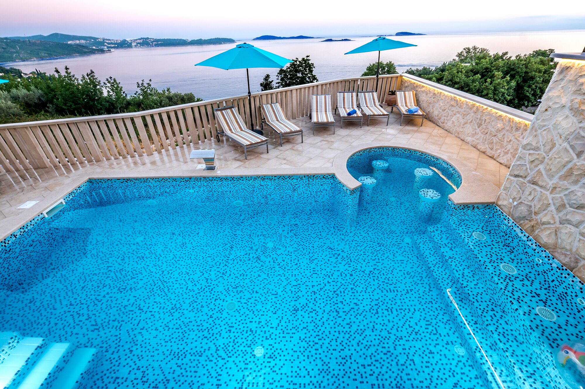 Una piscina con vistas al mar, rodeada de sillones de descanso y sombrillas.
