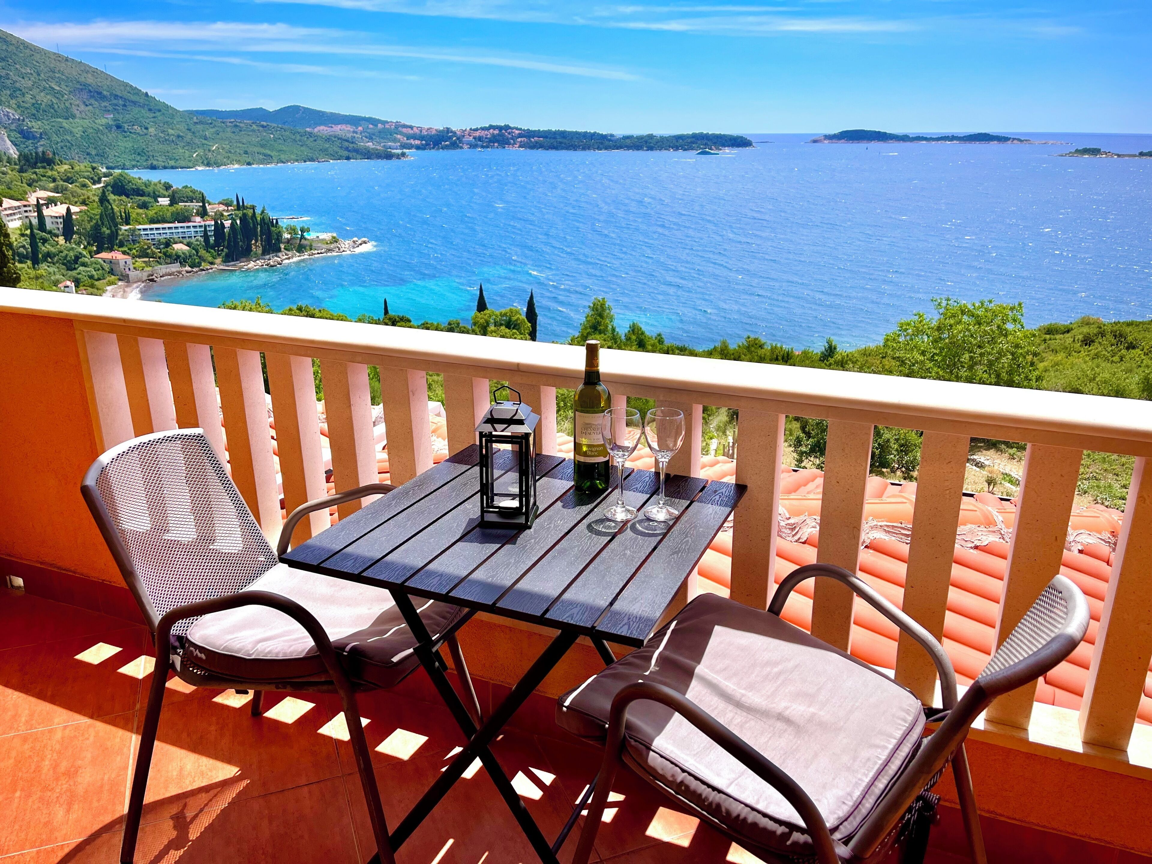 A balcony with a table, two chairs, a bottle of wine, and two glasses.