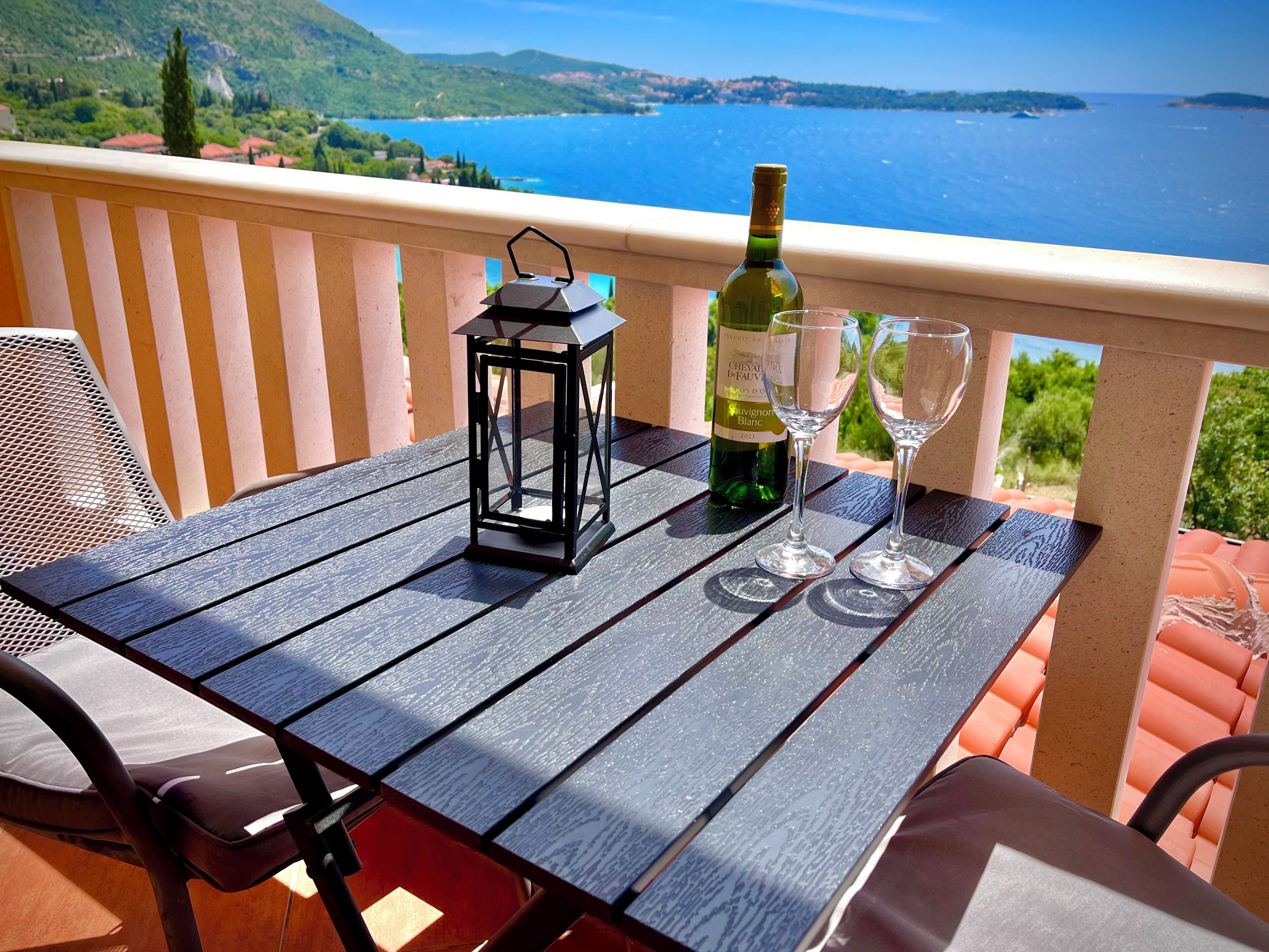 Une table avec une bouteille de vin, deux verres et une lanterne, le tout placé sur un balcon offrant une vue panoramique.
