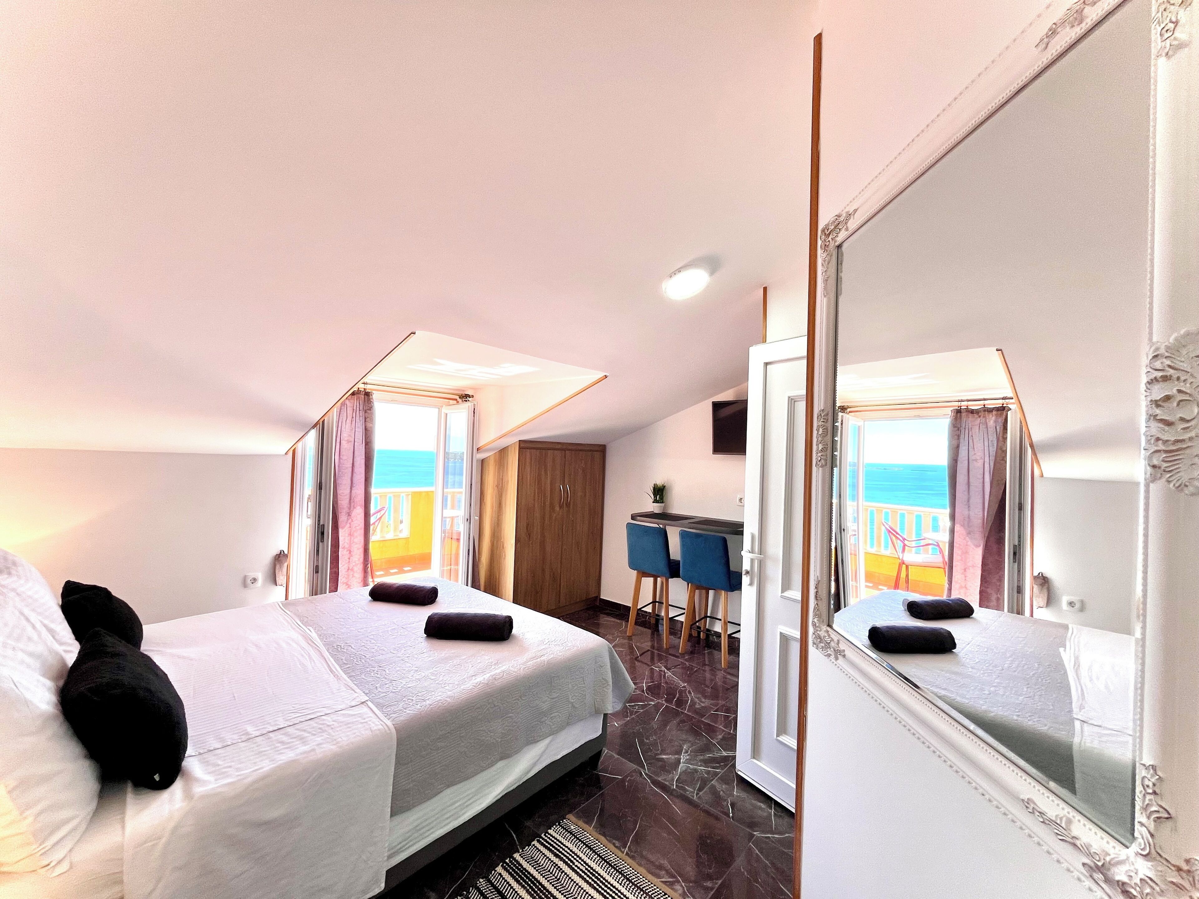 A hotel room with a bed, a desk, and a view of the sea.