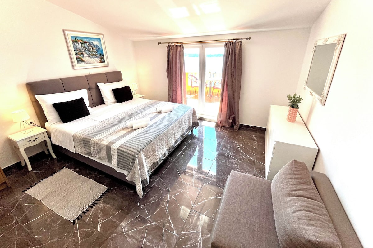 A hotel room with a bed, bedside table, lamp, and a small potted plant.