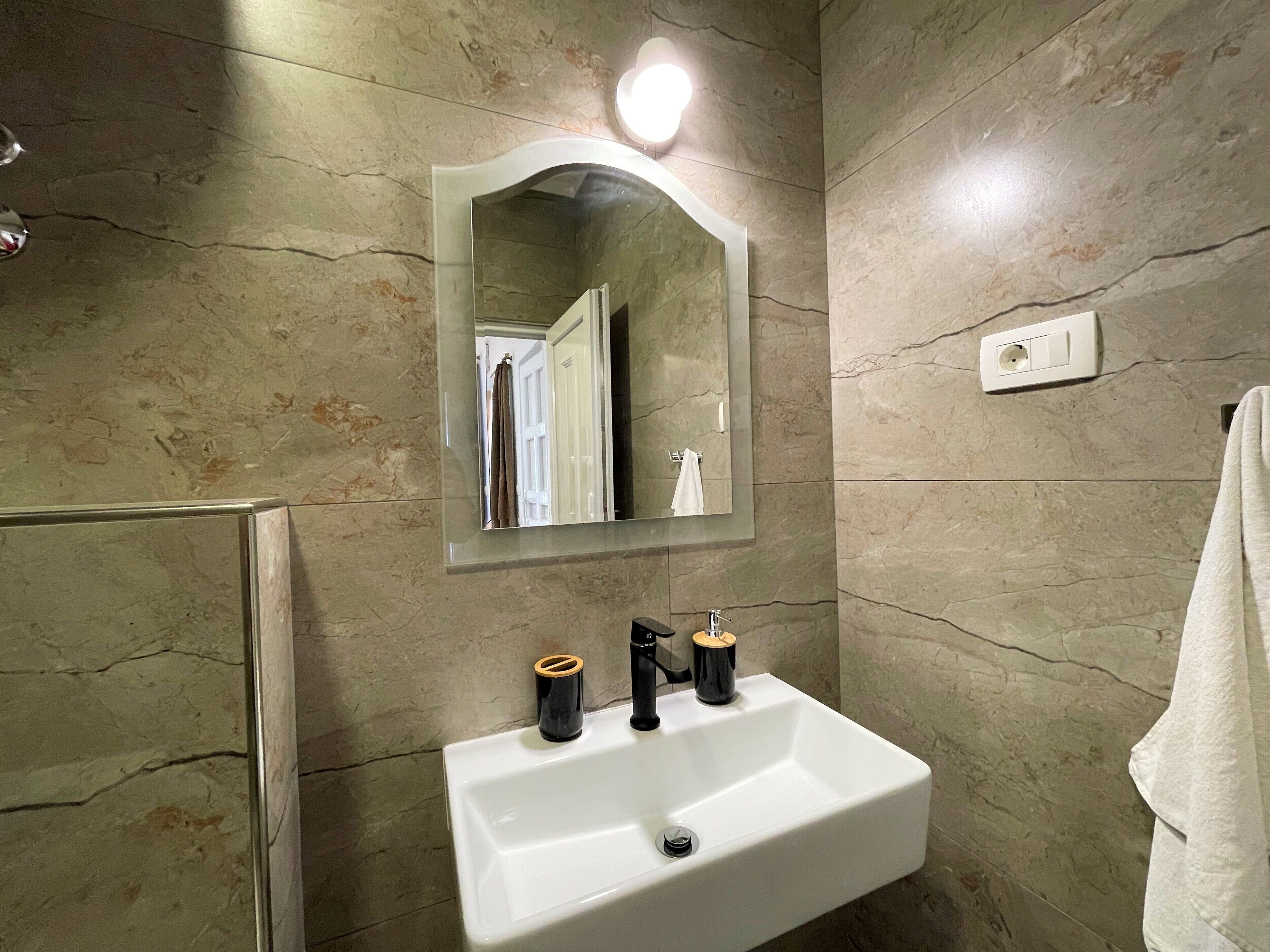 Un baño con lavamanos blanco, espejo y ducha.