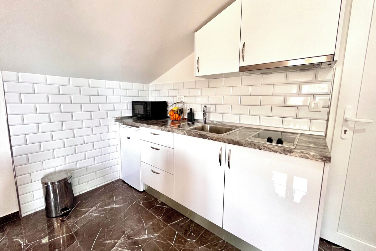 Una cocina moderna con armarios blancos, encimera de mármol y microondas negro.
