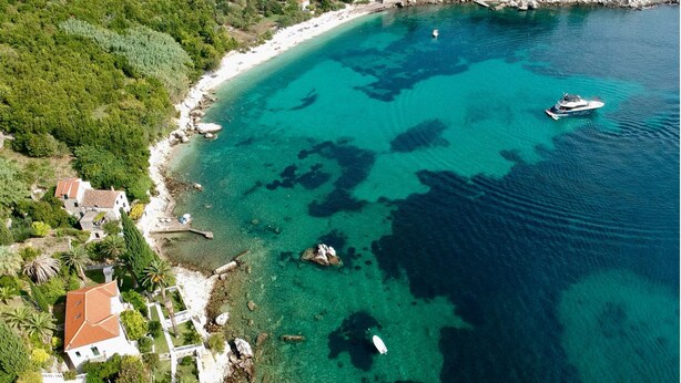 Vista aérea de una zona costera con playa, aguas turquesas cristalinas y un barco.
