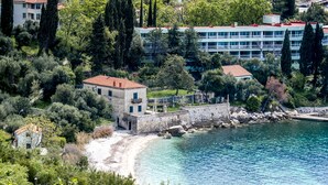 Un edificio costero con pared de piedra, junto a una playa y aguas azules cristalinas.