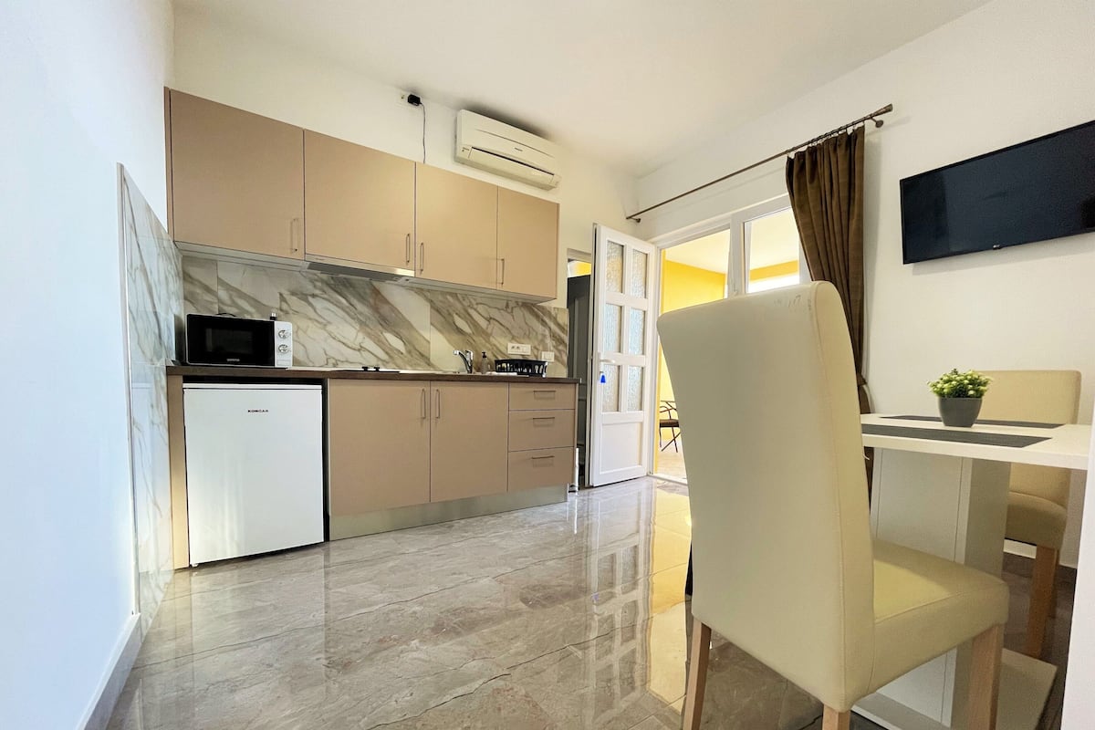 A modern kitchen with a built-in microwave, a small refrigerator, and a marble backsplash.